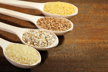 various cereals in wooden spoons on a brown wooden table