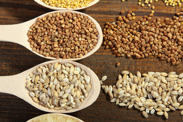 various cereals in wooden spoons and crumbled on a brown wooden table