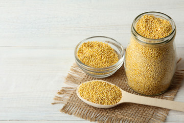 wheat cereal in glass  jar  with wooden spoon and glass bowl on a burlap on a white wooden table