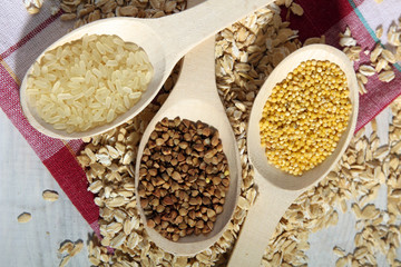 various cereals in wooden spoons on a white wooden table