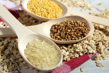 various cereals in wooden spoons on a white wooden table