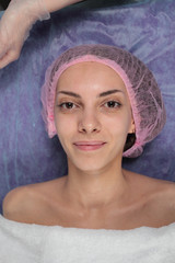 Closeup Girl is before the Procedure Facial Mask in Beauty salon. Spa Woman before applying Facial clay Mask. Beauty Treatments. Beautiful girl in cap on her head before applying facial mask.
