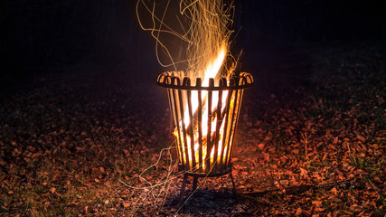 Photo de nuit de bois brûlant étincelant dans un panier à feu sur un sol forestier feuillu en automne