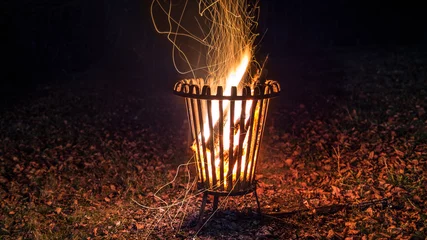 Papier Peint photo Lavable Flamme Photo de nuit de bois brûlant étincelant dans un panier à feu sur un sol forestier feuillu en automne