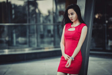 Beautiful Asian girl model in red dress posing at the modern glass style city background. 