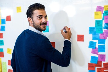 Young man smiling at camera while writing on white board