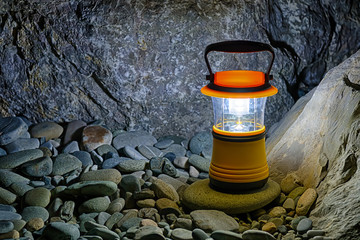 Luminous hand lantern standing on pebble near bouldeers, HDR processing.