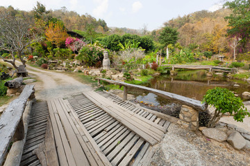 Big wooden bridge over river in old Thai village with trees around
