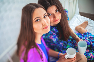 Close up indoor lifestyle portrait of two pretty cheerful girls holds cup of coffee .