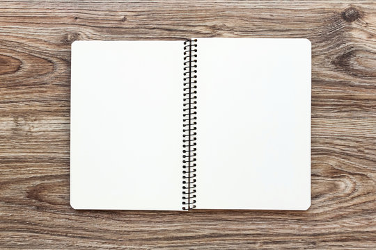 Mockup of open notepad with blank pages on wooden background.