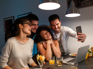 Friends sitting together in living room and watching movie on on laptop and taking selfie