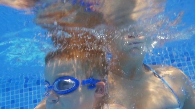 Slow motion shot of young woman and little boy in goggles taking breath and diving under water in pool.