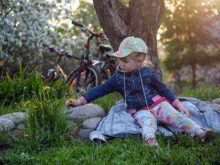 Cycling. A child sitting on the jacket resting in the grass. Girl considers flower dandelions....