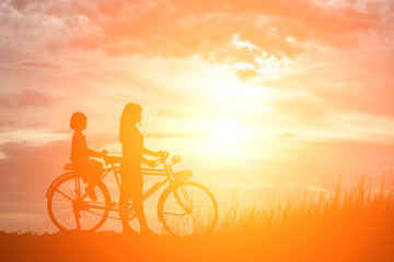 Silhouette of mother and daughter biking at sunset happy time