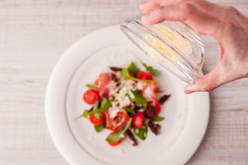 Woman pours a glass plate of cheese in a salad of tomatoes and h