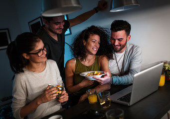 Friends sitting together in living room and watching movie on on laptop and chatting