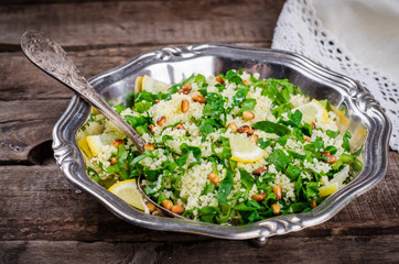 Couscous salad with parsley and pine nuts in vintage bowl on wooden background. Selective focus. Toned image