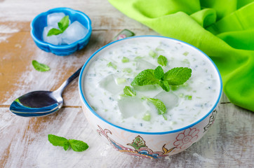 Tzatziki or cacik, cold cucumber and yogurt soup or salad with mint leaves on wooden background. Selective focus