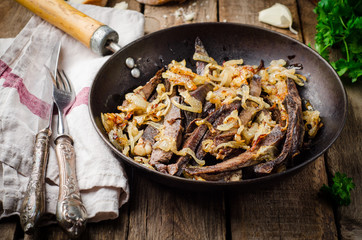 Roasted beef heart in vintage iron pot on wooden background. Selective focus