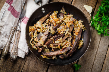 Roasted beef heart in vintage iron pot on wooden background. Selective focus