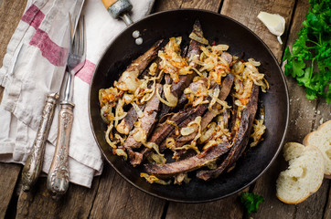 Roasted beef heart in vintage iron pot on wooden background. Selective focus