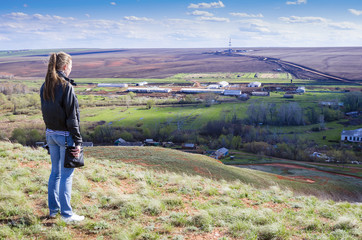 Girl looks from a hill on a rural landscape with drilling rigs in the field - obrazy, fototapety, plakaty