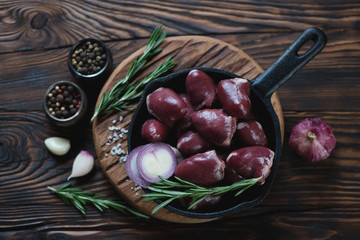 Frying pan with raw fresh turkey hearts and condiments, top view