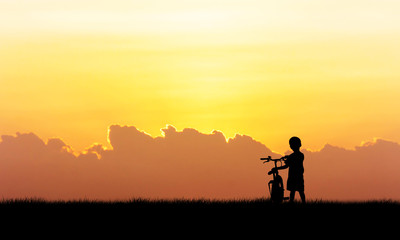 Fototapeta premium Silhouette of little boy standing hold bicycle sunset background