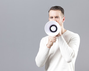 Young man shouting with a megaphone on grey background