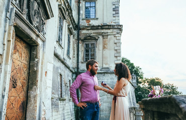 A young couple. Man giving a ring woman, love, couple, date. Man with a beard and dressed stylishly does offer Curly girl. Couple near old castle.