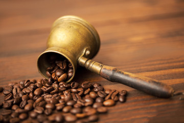 coffee beans spill out of cezve, on the wooden background