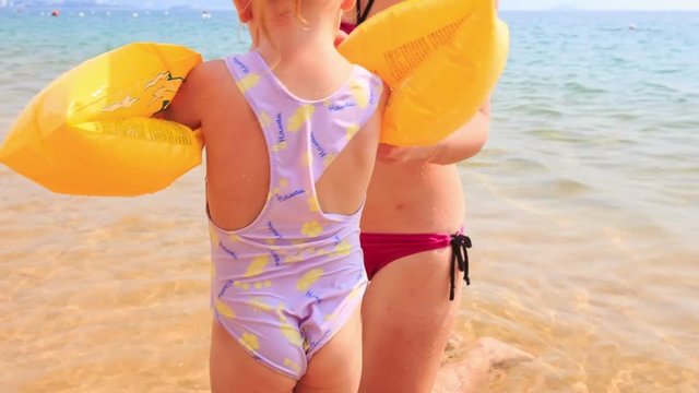 Mother Puts Safety Armbands on Daughter on Sand Beach