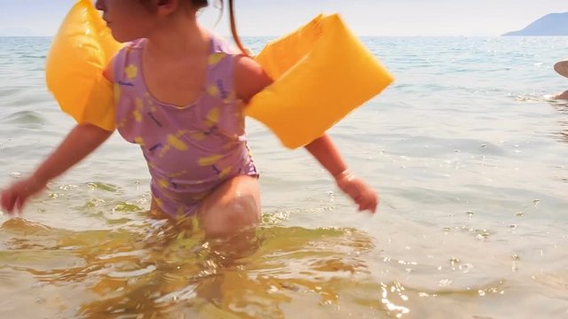 Closeup Little Girl in Armbands Goes out of Sea to Beach