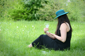 Beautiful young woman sittting in the grass and holding empty glass