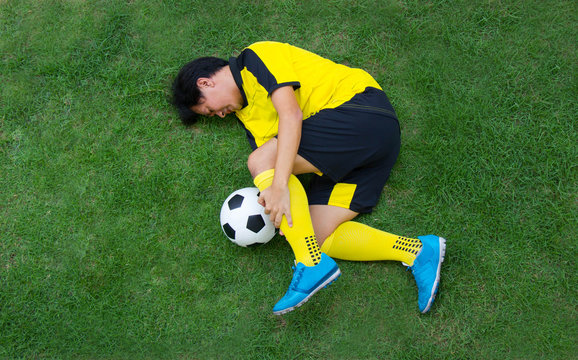 Football player in Yellow lying injured on the pitch.