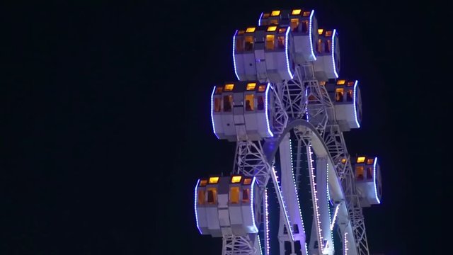 Close-up of Noria by rotating at night with large colorful of led lights and motion.Slow backward turns and stops.