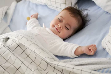 Fototapeten Smiling baby girl lying on a bed sleeping on blue sheets © javiindy