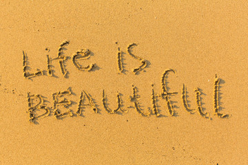 Fototapeta na wymiar Life is beautiful - text written on sandy beach.