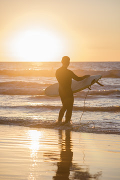Silhouette of a surfer in front of sun with board during sunset in San Diego, California, with creative flare
