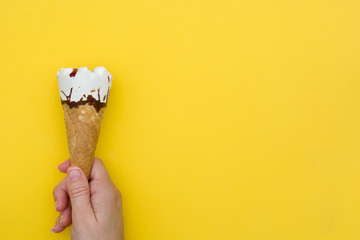Hand holding ice cream cone on yellow background
