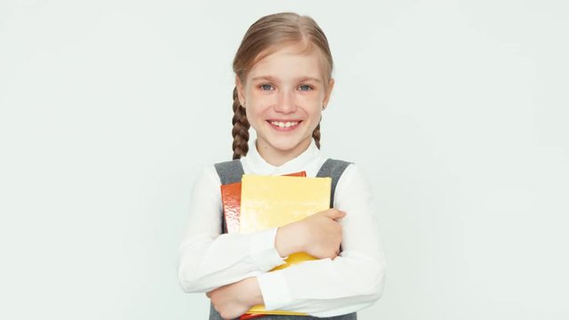 Cute happy schoolgirl 7-8 years hugging books on white background smiling with teeth at camera