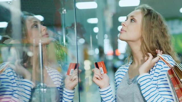 Attractive young woman looking at a glass display case in the store. The hands holding the card for shopping and shopping bags