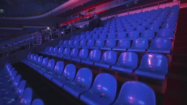 Many rows of blue and red empty seats in the stadium. Behind the scenes, concert preparation.