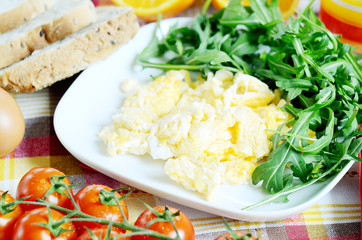 Scrambled eggs, toast bread, fresh juice, tomatoes and oranges