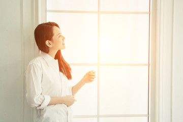 Young beautiful woman standing against window watching at sunris