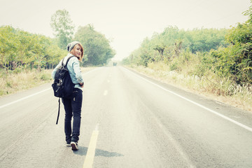 Rear view of a young woman hitchhiking carrying backpack walking