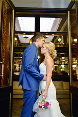 Wedding couple indoors is hugging each other. Beautiful model girl in white dress. Man in suit. Beauty bride with groom. Female and male portrait. Woman with lace veil. Cute lady and handsome guy