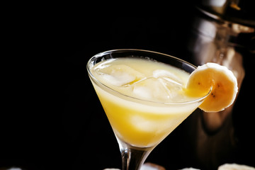 Yellow cocktail with whiskey, banana and ice, black background,