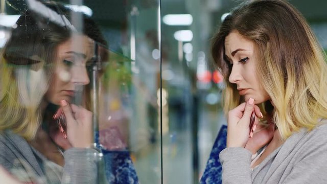 Portrait of a sad young woman standing near shop window, holding the payment card in the hands of