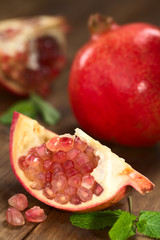 Granatapfelstück (lat. Punica granatum) mit ganzer Granatapfel im Hintergrund (Selektiver Fokus, Fokus auf die oberen Samen)